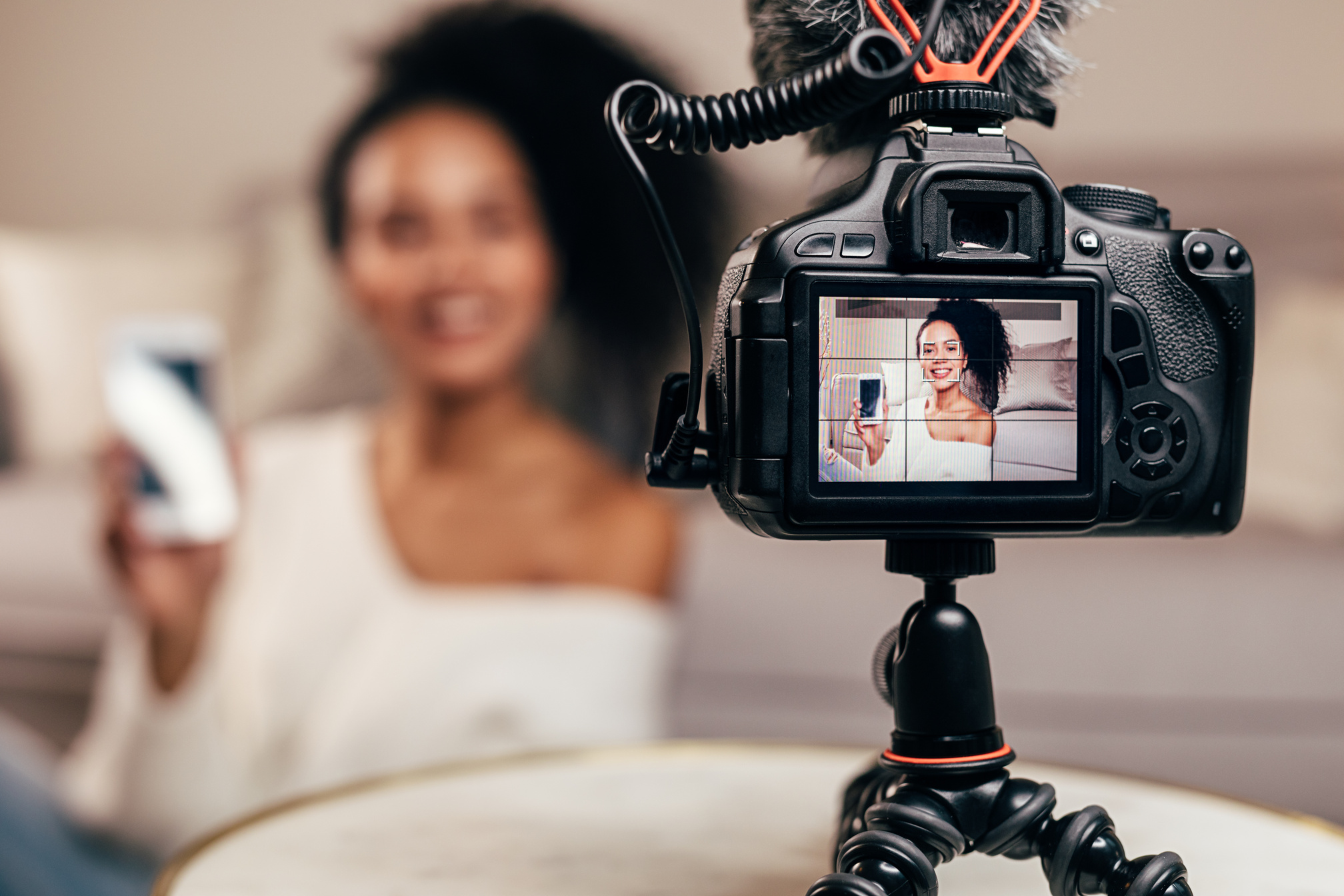 Closeup of DSLR camera screen showing a young vlogger holding a smartphone